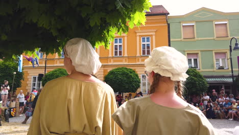 Cámara-Lenta-De-Dos-Campesinas-Vestidas-Con-Ropa-Barata-Viendo-A-Los-Caballeros-Pelear-En-La-Plaza-Principal,-Recreación-Medieval,-Festival-Preludij-En-Slovenj-Gradec-Eslovenia