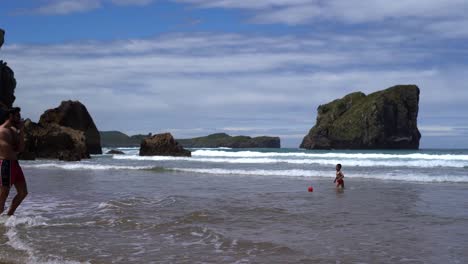 Man-Watching-Kid-Playing-Ball-In-Waves-During-Summer-Vacation,-Spain