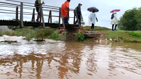 People-walking-in-rain-over-river-bridge,-continuous-low-angle-shot