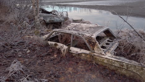 Pan-left-to-reveal-several-old-rusty-abandoned-cars-embedded-in-the-ground-on-the-river-bank-of-the-Knik-river-near-Eklutna-Tailrace-area-near-Palmer-Alaska