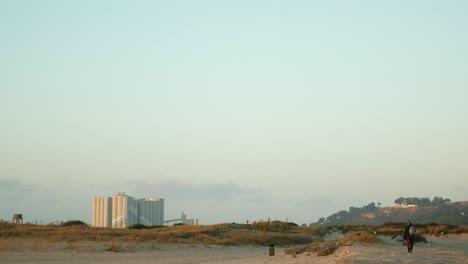 Lonely-fisherman-walking-away-from-the-beach-at-sunset,-wide-shot