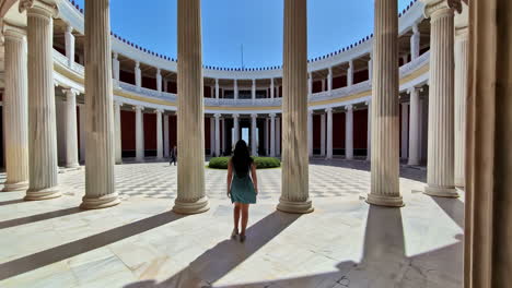 Following-shot-of-a-female-tourist-walking-into-an-open-Zappeio-hall,-Attica,-Greece-on-a-sunny-day