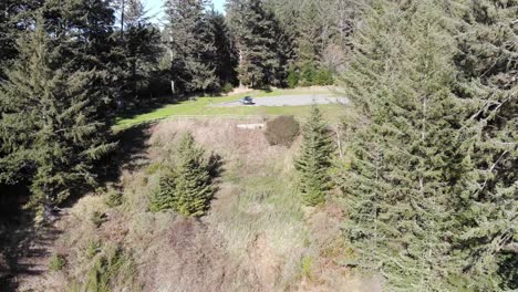 Drone-flies-backward-away-from-car-on-the-coast-near-a-cliff