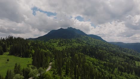 Aerial-wide-view-showing-tall-mountains-peaks-covered-in-dense-coniferous-green-forests,-overcast