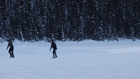 Toma-Panorámica-En-Cámara-Lenta,-Pareja-Patinando-Sobre-Hielo-En-Un-Lago-Congelado,-Parque-Nacional-Banff