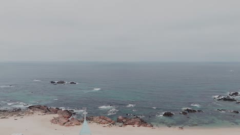 Aerial-view-of-a-rocky-coastline-with-a-sandy-beach-and-calm-ocean-waves