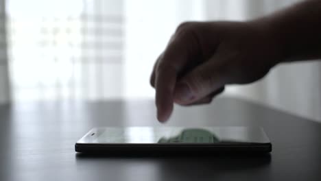 Close-up-male-hand-using-smartphone-scrolling-the-touchscreen-on-table