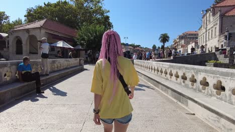 Back-view-of-a-young-woman-traveler-walking-across-a-bridge-in-the-historic-old-town-of-Dubrovnik,-Croatia,-capturing-the-essence-of-adventure-and-cultural-exploration