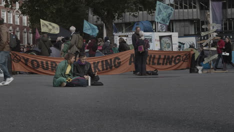 Extinction-Rebellion-Demonstration-In-Der-Victoria-Street-Am-Westeingang-Der-Westminster-Abbey-Mit-Zwei-Demonstrantinnen,-Die-Auf-Dem-Bürgersteig-Sitzen