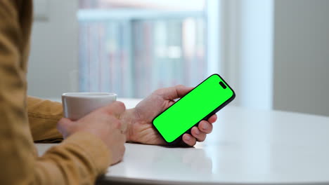 Man-in-brown-shirt-holding-coffee-cup-and-smartphone,-green-screen-video-template