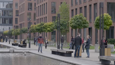 Urban-park-scene-with-diverse-people-walking-and-sitting,-modern-architecture,-cloudy-day,-tilt-down-camera-movement