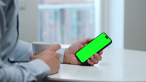 Man-in-light-blue-shirt,-coffee-cup,-smartphone,-vertical-mode,-green-screen