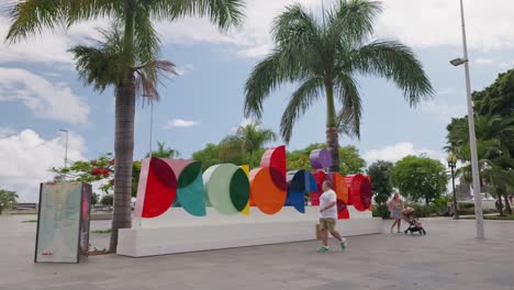 Colorful-outdoor-Madeira-sign-with-palm-trees-and-people-walking-by-under-a-bright-blue-sky