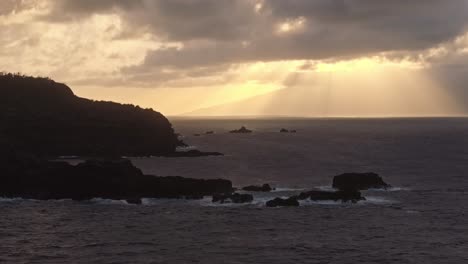 Low-aerial-shot-of-rocky-coast-silhouetted-against-a-cloudy-sky-with-rays-of-light-beaming-through