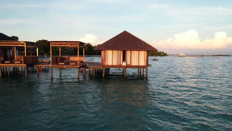 young-asian-woman-enjoying-vacation-and-sitting-at-a-wooden-overwater-villa-at-sunrise-at-Leebong-Island-in-Belitung-Indonesia,-Aerial