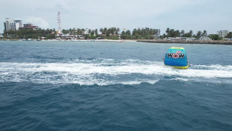 Young-Couple-Enjoy-Water-Tubing-Activity-on-Island-Vacation,-FPV-Drone-Follow-Shot