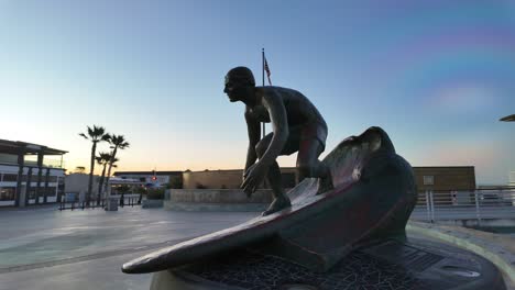 Sonnenaufgangssilhouette-Der-Tim-Kelly-Statue-In-Hermosa-Beach,-Schumacher-Plaza-Mit-Lebendigem-Himmel