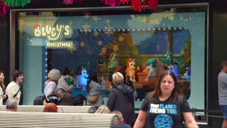 Bluey's-Christmas-display-on-Myer's-annual-Christmas-windows-in-bustling-downtown-Melbourne-City,-Bourke-Street-Mall,-with-pedestrians-passing-by-captured-in-slow-motion-shot