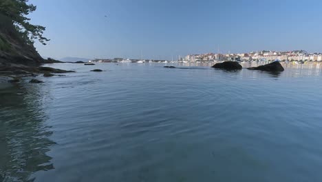 über-Dem-Wasser-Des-Strandes-Dämmert-Es-Mit-Der-Strahlenden-Sonne,-Die-Die-Gebäude-Und-Boote-An-Der-Küste-Beleuchtet,-Eine-Möwe-Fliegt-Tief-Und-Schießt-Schräg