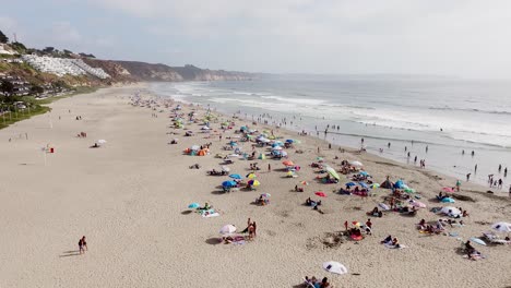 Aerial-Flying-Over-Maitencillo-beach-With-Beachgoers-And-Colourful-Parasols