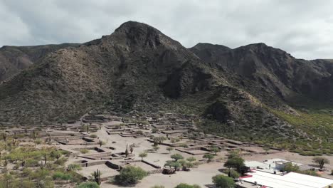 Aerial-view-above-Ciudad-Sagrada-de-Quilmes,-archaeologic-ruins-with-desert-mountain-landscape-in-Argentina