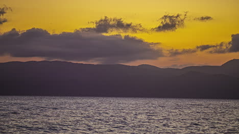 Der-Faszinierende-Zeitraffer-Des-Sonnenuntergangs-Zeigt-Wolken,-Meerwasser-Und-Berge-In-Atemberaubender-Harmonie