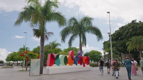 Colorful-Madeira-sign-with-palm-trees-and-people-walking-around-on-a-sunny-day