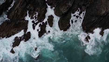 Vista-Aérea-A-Vista-De-Pájaro-De-Las-Olas-Del-Océano-Rompiendo-En-Las-Rocas-De-Byron-Bay,-Nueva-Gales-Del-Sur,-Australia