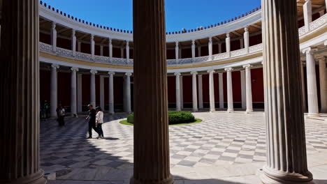 Los-Visitantes-Exploran-La-Arquitectura-Antigua-De-La-Sala-Zappeion-En-Atenas,-Grecia,-Bajo-Un-Cielo-Azul-Claro.