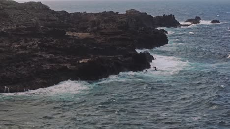 Low-aerial-view-of-black-jagged-rocks-along-the-coast-of-Maui-in-Hawaii