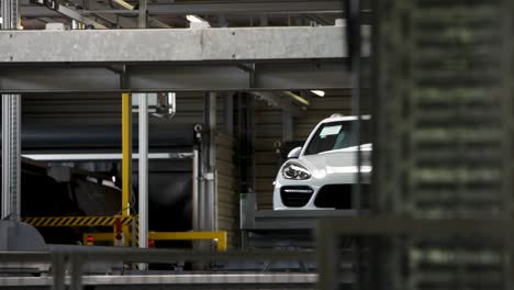 White-car-on-an-assembly-line-in-a-modern-automotive-factory,-visible-through-industrial-shelving