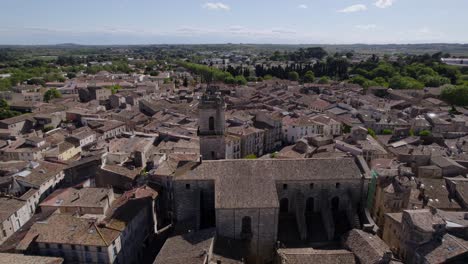 aerial-drone-shot-over-a-village-with-the-beautiful,-imposing-church-in-the-middle,-the-hundreds-of-light-colored-roofs-of-the-surrounding-houses,-a-few-trees-and-greenery-in-the-background,-blue-sky