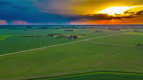 Colorful-sunset-and-a-distant-storm-over-farmland-crops---aerial-hyper-lapse