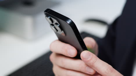 Close-up-of-male-hands-typing-on-dark-blue-smartphone-with-three-camera-lenses