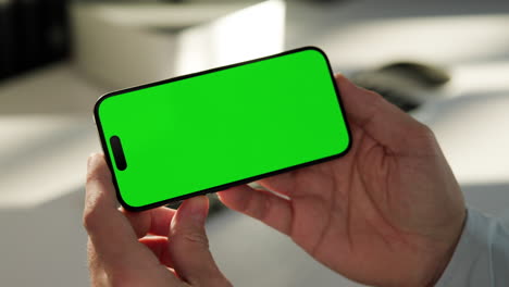 Close-up-of-hands-holding-smartphone-in-landscape-mode,-green-screen-template