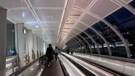 People-walking-on-an-airport-moving-walkway-in-a-modern,-well-lit-terminal-at-night