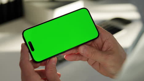 Two-hands-holding-smartphone-in-landscape-mode,-green-screen-video