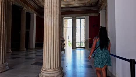 A-woman-in-a-blue-dress-walks-inside-the-grand,-columned-interior-of-Zappeion-Hall-in-Athens