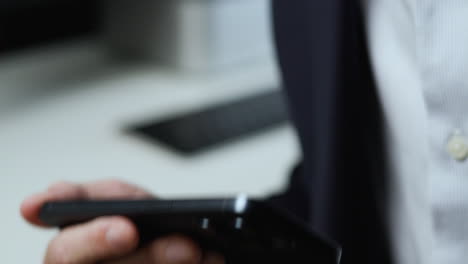 Man-in-dark-blue-jacket-and-light-blue-pin-stripe-shirt-holding-smartphone