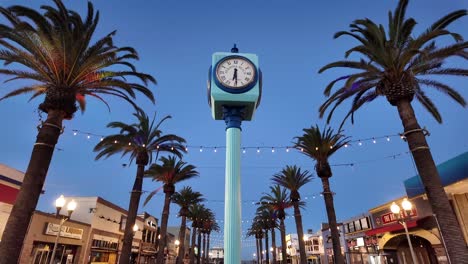 Crepúsculo-En-La-Playa-Hermosa-Con-Palmeras-Iluminadas-Y-El-Reloj-De-La-Plaza-Schumacher