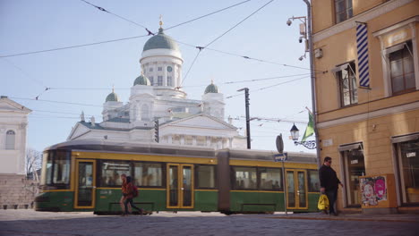 Teleobjektiv-Straßenansicht-Der-Kathedrale-Von-Helsinki-Mit-Vorbeifahrenden-Menschen-Und-Einer-Straßenbahn