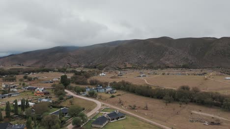 Scenic-aerial-above-Tafì-del-Valle-city-surrounded-by-cloudy-mountain-landscape,-Argentina