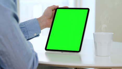 Man-with-blue-shirt,-tablet,-portrait-mode,-green-screen,-table-with-coffee-cup