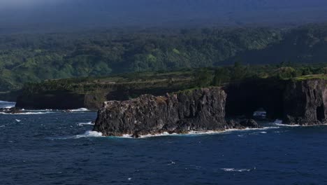 Wide-aerial-orbiting-view-of-black-rock-formation-jutting-out-into-the-ocean-off-the-coast-of-Maui's-north-shore