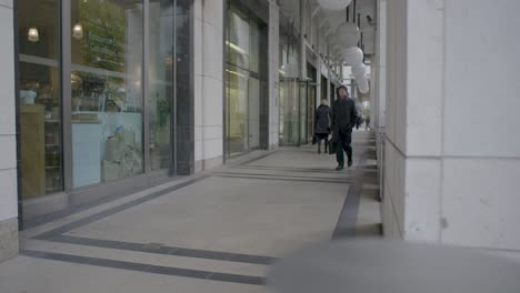 Quiet-city-walkway-with-pedestrians-passing-by-a-restaurant,-captured-during-daytime-with-clear-lighting-and-a-modern-architectural-backdrop