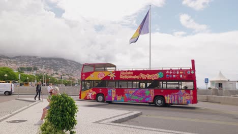 Colorful-tour-bus-in-Funchal,-Madeira-with-mountains-and-a-cloudy-sky-in-the-background