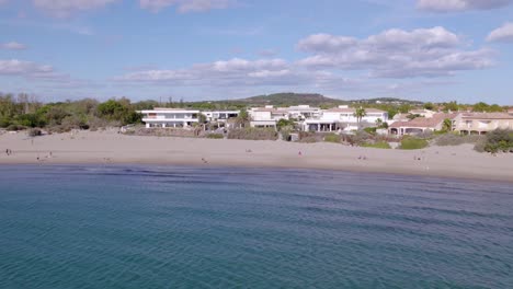 Tiro-Lento-Con-Plataforma-Rodante-Hacia-Apartamentos-De-Lujo-Frente-Al-Mar-En-Sete-Con-Gente-En-La-Playa.