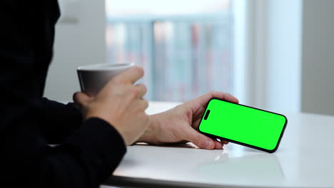 Green-screen-smartphone-template,-man-drinking-coffee,-holding-phone,-landscape