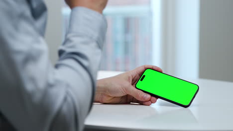 Man-in-light-blue-shirt,-smartphone,-coffee-cup,-landscape-mode,-green-screen