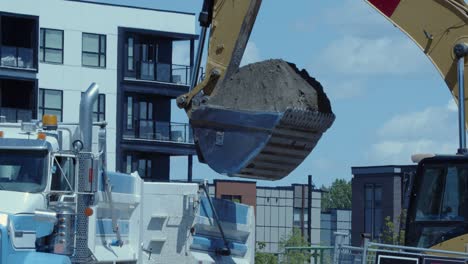 Excavator-at-urban-construction-site-dumps-dirt-into-heavy-truck-box